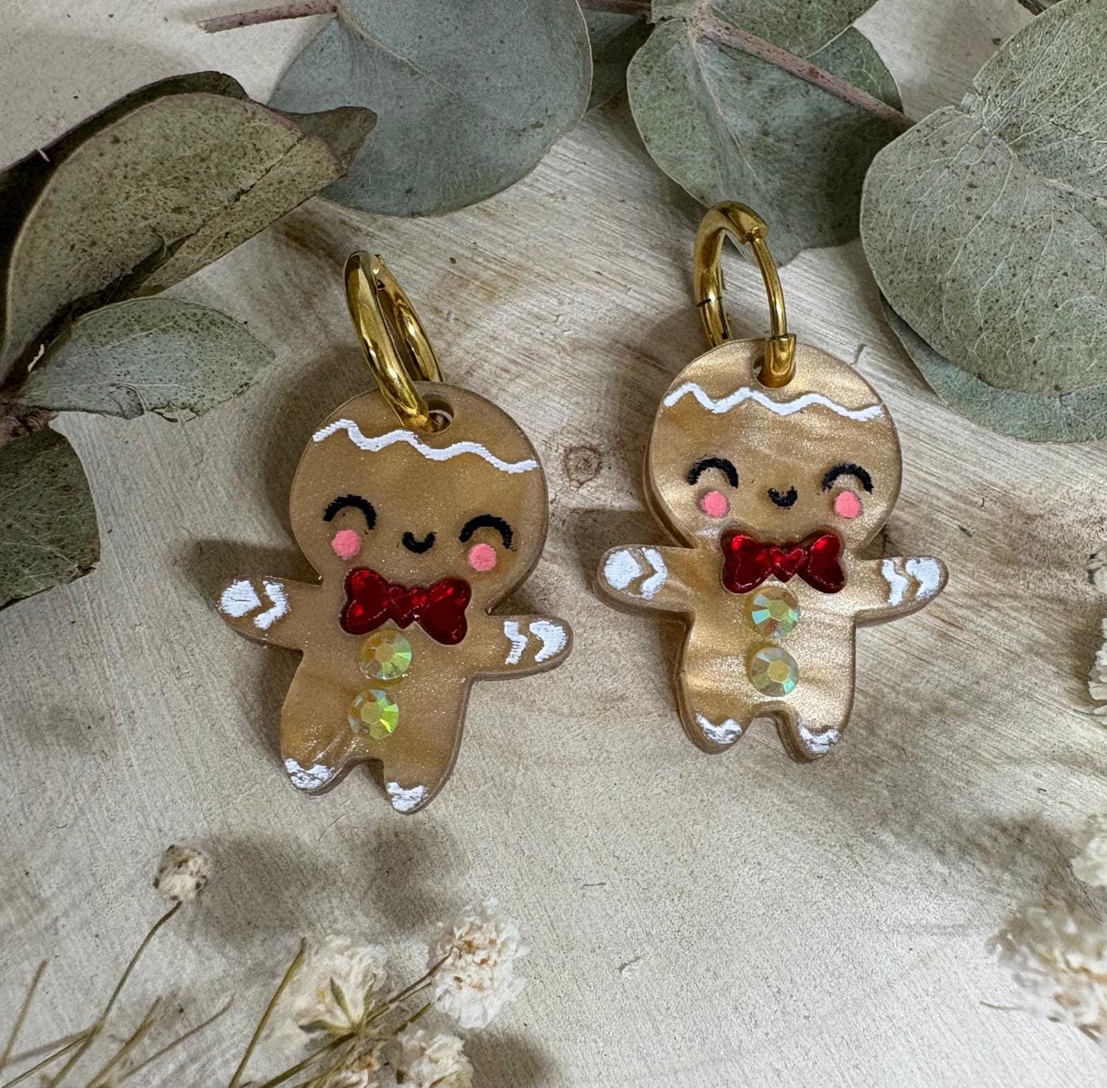 Los Pendientes Galleta de Jengibre llegan a Judithconalma para convertirse en uno de los accesorios más adorables y originales de esta Navidad. Inspirados en el icono más dulce de las fiestas, estos pendientes combinan ternura, brillo y ese toque totalmente artesanal que caracteriza nuestras colecciones navideñas. Fabricados en metacrilato de alta calidad con acabado perlado y detalles pintados a mano, cada galletita tiene un encanto único: mejillas sonrosadas, sonrisa adorable y un lazo rojo efecto espejo que aporta un toque festivo espectacular. Una pieza luminosa y superligera, diseñada para brillar en cenas, quedadas familiares, sesiones de fotos navideñas o cualquier look especial de estas fiestas.