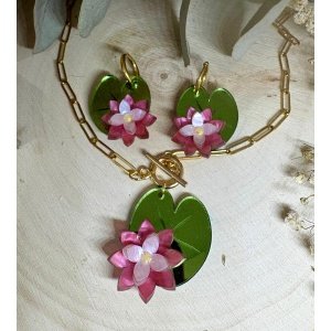 Inspirado en la delicadeza de las flores que flotan sobre el agua, el conjunto Pendientes y Colgante Nenúfar es una pieza elegante, fresca y llena de personalidad. Un diseño floral que evoca la calma de los jardines acuáticos y la belleza natural de los nenúfares. Cada elemento de este conjunto ha sido creado con mimo y atención al detalle, combinando metacrilatos de importación de alta calidad con un diseño cuidado que aporta volumen, textura y un juego de colores muy especial. Diseño exclusivo JudithconAlma Las flores en tonos rosados se apoyan sobre hojas verdes con acabado brillante que recuerdan a las hojas flotantes de los nenúfares, creando un conjunto armonioso, romántico y muy original.