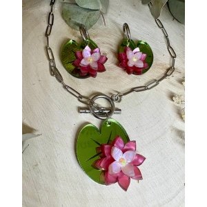 Inspirado en la delicadeza de las flores que flotan sobre el agua, el conjunto Pendientes y Colgante Nenúfar es una pieza elegante, fresca y llena de personalidad. Un diseño floral que evoca la calma de los jardines acuáticos y la belleza natural de los nenúfares. Cada elemento de este conjunto ha sido creado con mimo y atención al detalle, combinando metacrilatos de importación de alta calidad con un diseño cuidado que aporta volumen, textura y un juego de colores muy especial. Diseño exclusivo JudithconAlma Las flores en tonos rosados se apoyan sobre hojas verdes con acabado brillante que recuerdan a las hojas flotantes de los nenúfares, creando un conjunto armonioso, romántico y muy original.