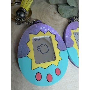 Llavero Tamagotchi personalizado Si los Pendientes Tamagotchi ya eran pura nostalgia, este Llavero Tamagotchi lleva el recuerdo de los años 90 un paso más allá. Inspirado en el mítico dispositivo del clásico Tamagotchi, este llavero reproduce su forma icónica con un diseño colorido, divertido y lleno de personalidad. Fabricado con metacrilatos espejo, pastel e iridiscentes, este llavero destaca por su brillo y por el contraste de colores que recuerdan al diseño original del juguete. En el centro aparece grabado uno de los personajes más conocidos del universo Tamagotchi, convirtiéndolo en un accesorio perfecto para fans del retro gaming, la cultura pop de los 90 y los complementos originales. Además de ser un llavero llamativo, también es ligero, resistente y perfecto para llevar en tus llaves, mochila o bolso, añadiendo siempre un toque divertido y nostálgico.