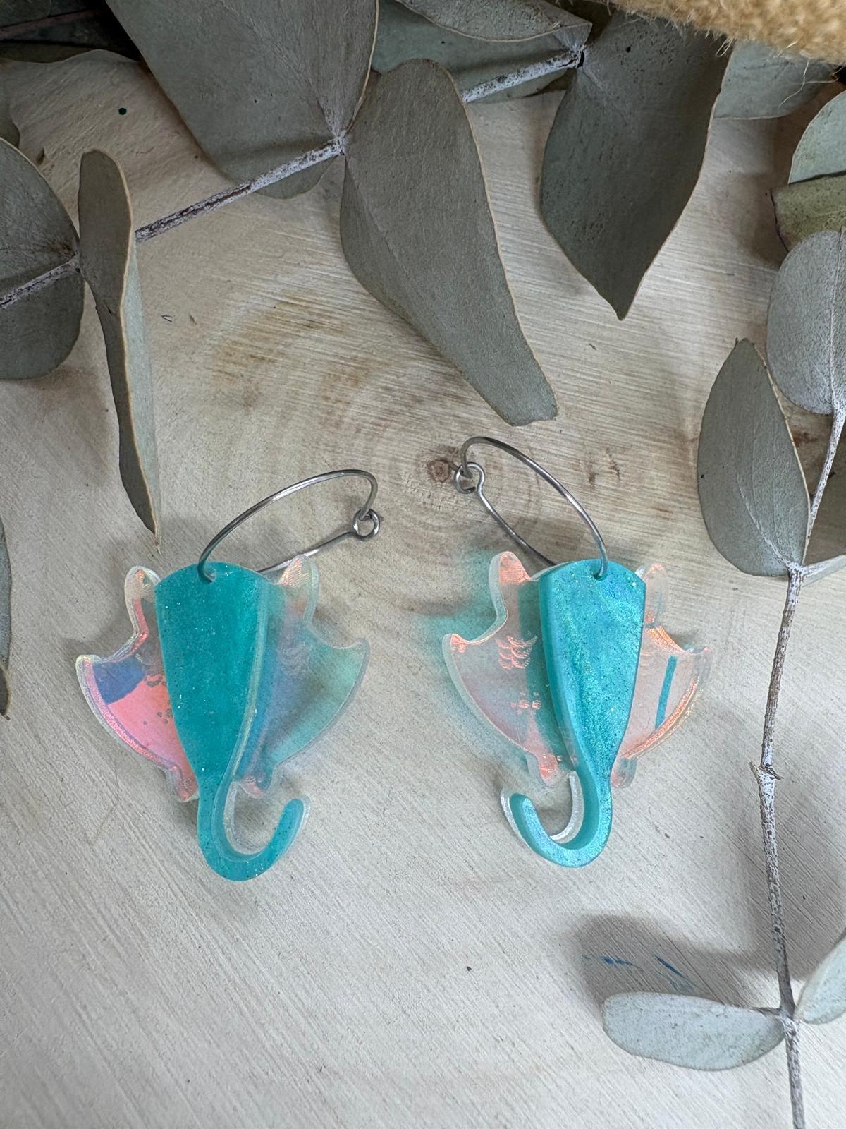 Pendientes Manta Raya – Colección Verano 2026 Los Pendientes Manta Raya de Judith con Alma son una pieza original y elegante inspirada en la belleza y la libertad del océano. Su diseño exclusivo reproduce la silueta de una manta raya en movimiento, creando unos pendientes únicos que evocan el mar, el verano y los días de playa. Fabricados artesanalmente con metacrilatos de importación de alta calidad, combinan un espectacular tono turquesa marmoleado con un metacrilato iridiscente que refleja diferentes colores según la luz. El resultado es una joya ligera, llamativa y llena de personalidad que no pasa desapercibida. Cada pendiente está cortado con tecnología láser de alta precisión, consiguiendo acabados limpios y detalles perfectamente definidos. Su tamaño de 3 x 3 cm (sin aro) los convierte en un complemento cómodo y versátil para el día a día, mientras que el aro fino plateado de 2 cm aporta un toque moderno y elegante. Estos pendientes forman parte de la exclusiva Colección Verano 2026 de Judith con Alma, una colección inspirada en el mar, la costa y la naturaleza marina. Son ideales para completar un look veraniego, para tus vacaciones, una cena junto al mar o simplemente para aportar frescura y originalidad a cualquier conjunto. Si buscas pendientes originales de metacrilato, pendientes inspirados en el mar o complementos artesanales diferentes, los Pendientes Manta Raya son la elección perfecta. Características principales Diseño exclusivo Judith con Alma. Inspirados en las mantas raya y el mundo marino. Fabricados con metacrilatos de importación de alta calidad. Combinación de metacrilato turquesa y efecto iridiscente. Corte láser de alta precisión. Muy ligeros y cómodos de llevar. Medida de la figura: 3 x 3 cm. Aro fino plateado de 2 cm. Ideales para looks de verano. Pieza artesanal realizada en pequeñas series. Colección Verano 2026.