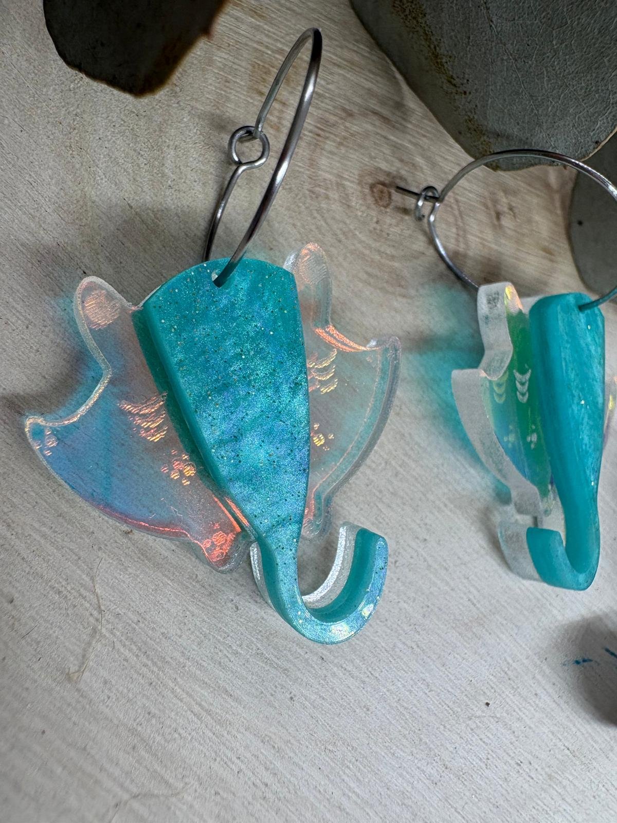 Pendientes Manta Raya – Colección Verano 2026 Los Pendientes Manta Raya de Judith con Alma son una pieza original y elegante inspirada en la belleza y la libertad del océano. Su diseño exclusivo reproduce la silueta de una manta raya en movimiento, creando unos pendientes únicos que evocan el mar, el verano y los días de playa. Fabricados artesanalmente con metacrilatos de importación de alta calidad, combinan un espectacular tono turquesa marmoleado con un metacrilato iridiscente que refleja diferentes colores según la luz. El resultado es una joya ligera, llamativa y llena de personalidad que no pasa desapercibida. Cada pendiente está cortado con tecnología láser de alta precisión, consiguiendo acabados limpios y detalles perfectamente definidos. Su tamaño de 3 x 3 cm (sin aro) los convierte en un complemento cómodo y versátil para el día a día, mientras que el aro fino plateado de 2 cm aporta un toque moderno y elegante. Estos pendientes forman parte de la exclusiva Colección Verano 2026 de Judith con Alma, una colección inspirada en el mar, la costa y la naturaleza marina. Son ideales para completar un look veraniego, para tus vacaciones, una cena junto al mar o simplemente para aportar frescura y originalidad a cualquier conjunto. Si buscas pendientes originales de metacrilato, pendientes inspirados en el mar o complementos artesanales diferentes, los Pendientes Manta Raya son la elección perfecta. Características principales Diseño exclusivo Judith con Alma. Inspirados en las mantas raya y el mundo marino. Fabricados con metacrilatos de importación de alta calidad. Combinación de metacrilato turquesa y efecto iridiscente. Corte láser de alta precisión. Muy ligeros y cómodos de llevar. Medida de la figura: 3 x 3 cm. Aro fino plateado de 2 cm. Ideales para looks de verano. Pieza artesanal realizada en pequeñas series. Colección Verano 2026.